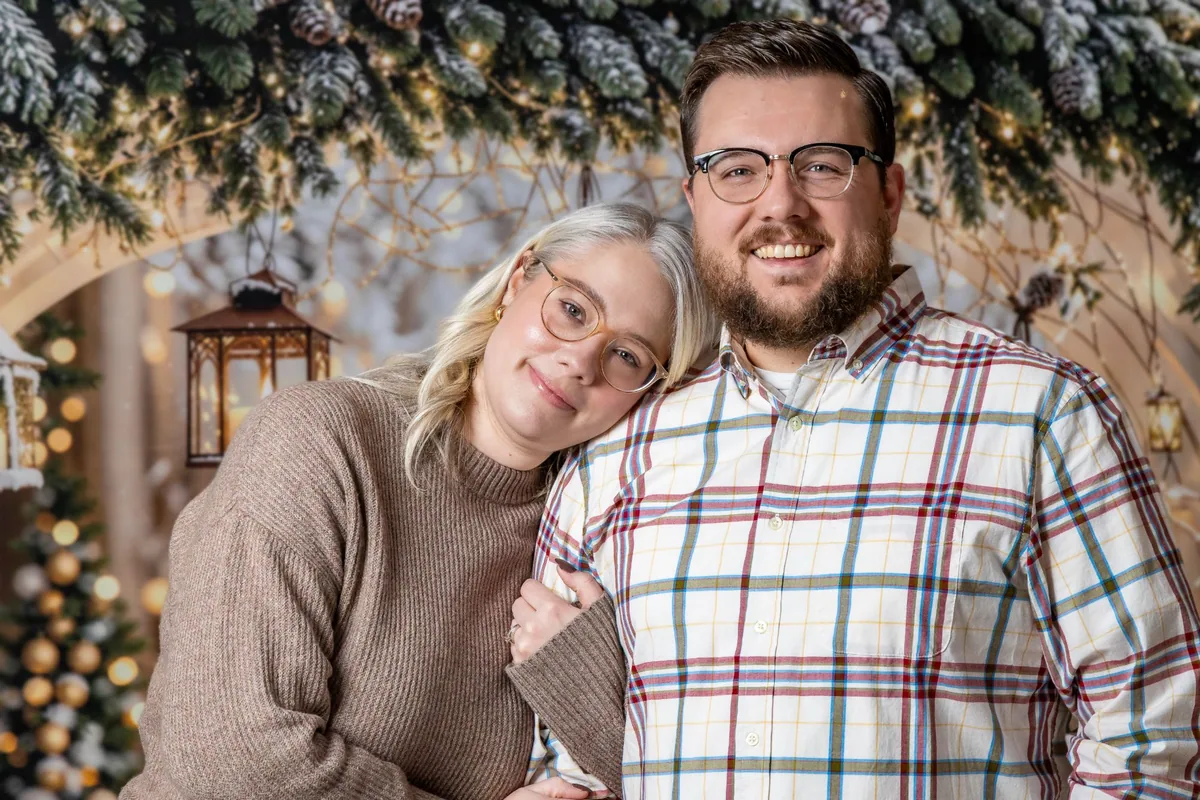 Smiling couple in cozy sweaters in front of the snowy pine garland backdrop