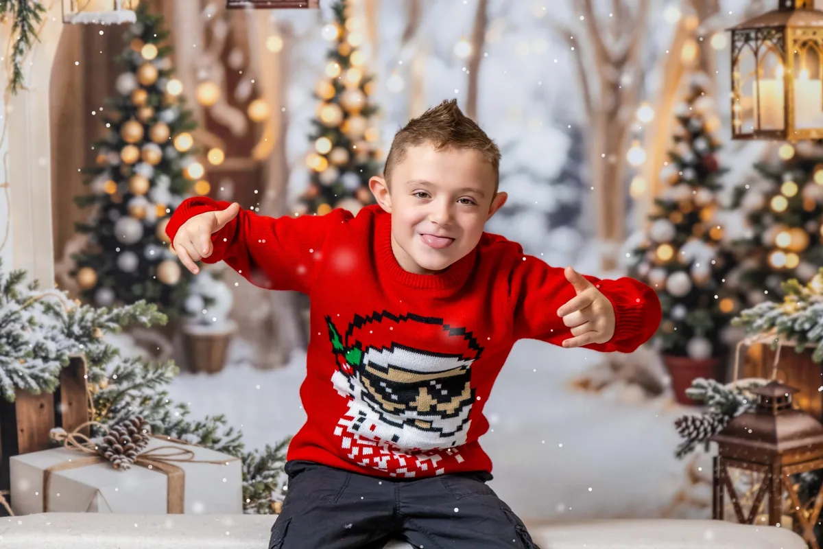 Playful boy in a red Santa sweater posing in front of the snowy Christmas trees