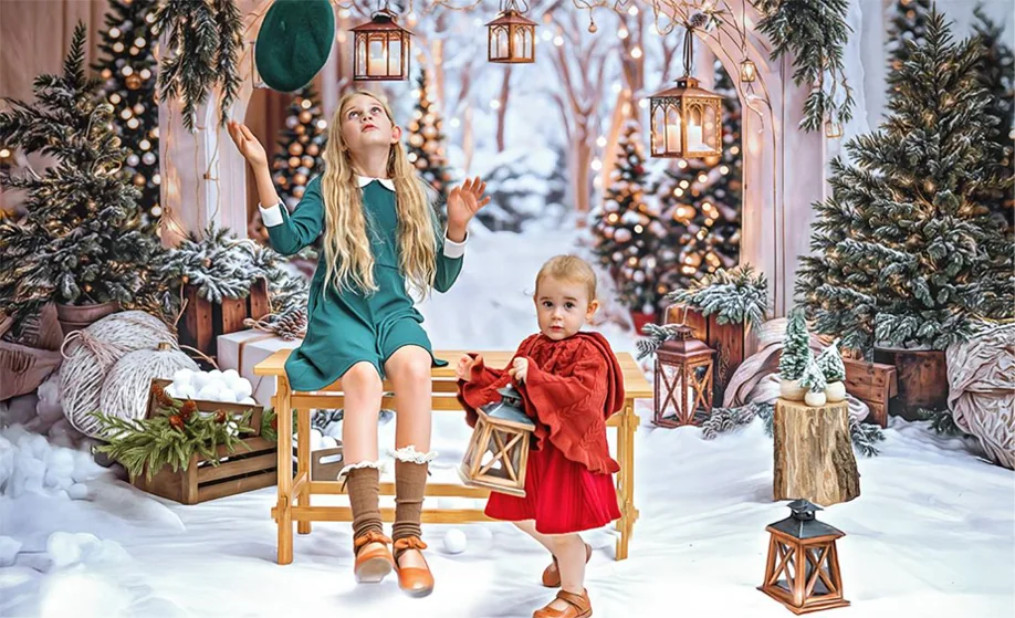 Girl in a teal dress and a toddler in red on a bench in the snowy Christmas set